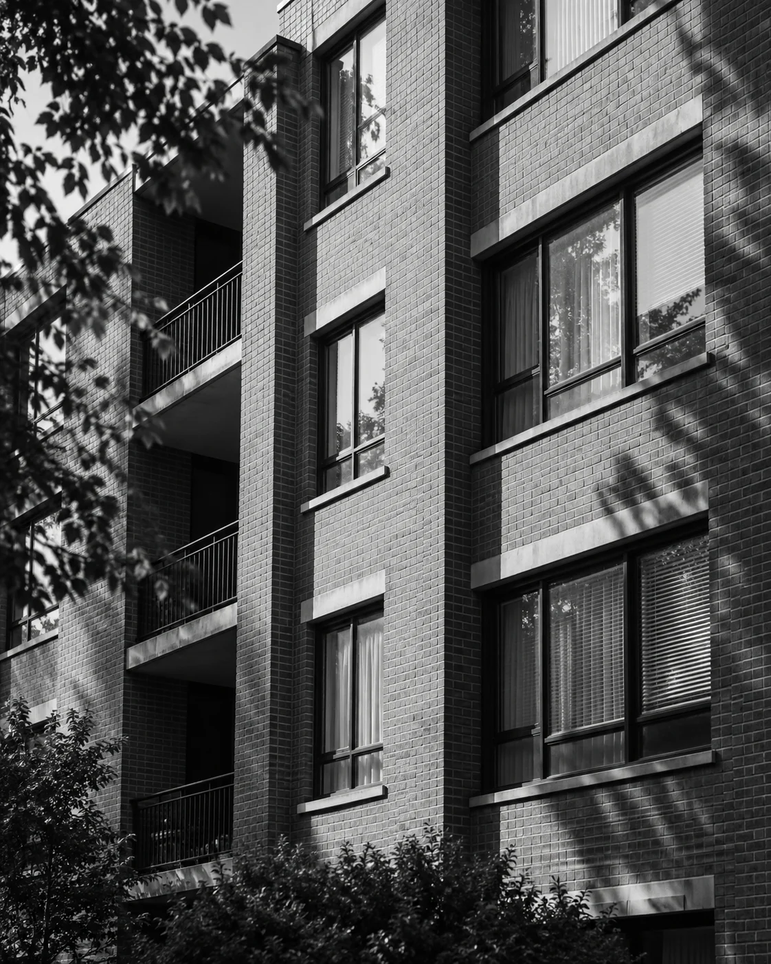 Black-and-white architectural study of brickwork, windows, and afternoon shadows on an apartment building.